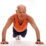 An older man wearing an orange vest holds a strong press-up pose